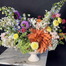 Large mixed flower arrangement in a white pedestal vase