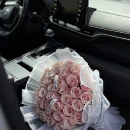 Bouquet of pale pink roses wrapped in white paper and ribbon on a car seat