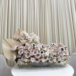 Large pastel floral arrangement with roses and orchids in a low gray bowl