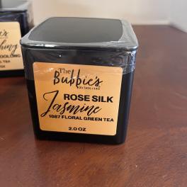 Square black tin of Rose Silk Jasmine floral green tea with gold label on a wooden surface