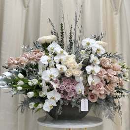 Large pastel floral arrangement with white orchids and blush roses in a black vase