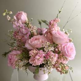 Pink roses and small blossoms arranged in a pale pedestal vase