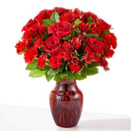 Red roses and carnations arranged in a red glass vase