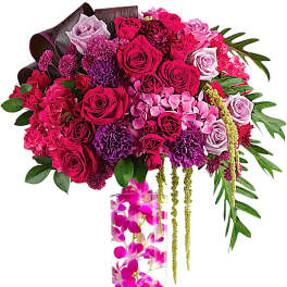Pink and purple rose arrangement in a tall clear vase with orchids
