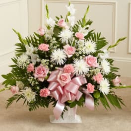 Fan-shaped arrangement of pink roses and carnations with white mums in a white container with pink bow
