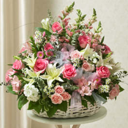 Pink and white basket arrangement with roses, lilies, carnations, and filler flowers in a white wicker basket.