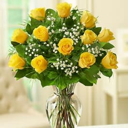 Arrangement of yellow roses with white filler flowers in a clear glass vase