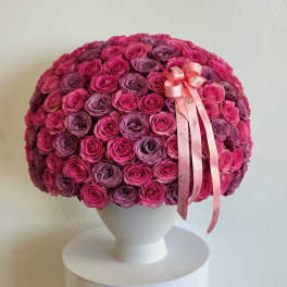 Round bouquet of pink and purple roses in a white vase with a pink ribbon