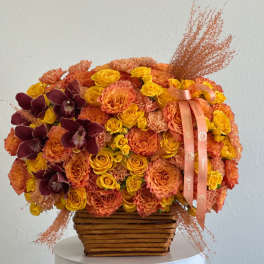 Orange and yellow floral arrangement in a woven basket with burgundy orchids