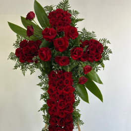 Cross-shaped arrangement of red roses with greenery on a stand