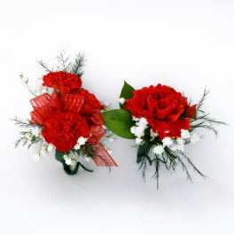 Pair of small red carnation corsages with white accent flowers and greenery