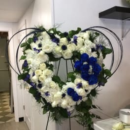 Heart-shaped floral wreath with white and blue roses on a stand