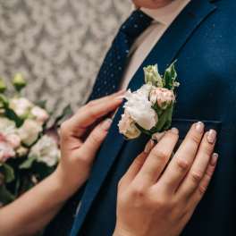 Boutonniere pinned to a navy suit jacket beside a woman's hands