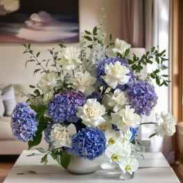 Blue hydrangeas and white orchids arranged in a white bowl vase