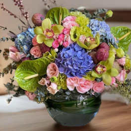 Colorful bouquet in a green glass vase with hydrangeas, roses, and orchids