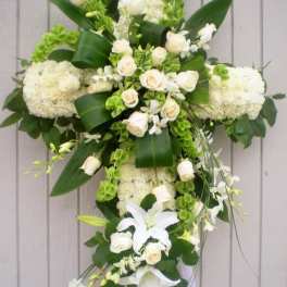 Tall white floral cross with roses, lilies, and green accents on a standing easel