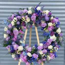 Large circular wreath of purple, blue, and white flowers on a wooden easel
