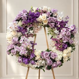 Large circular floral wreath on a wooden easel with purple, white, and cream blooms