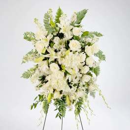 Standing spray of white roses, lilies, and other blooms with ferns on a metal easel.