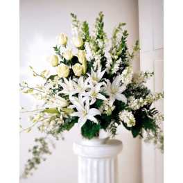Tall white arrangement of lilies and roses in a white urn on a pedestal