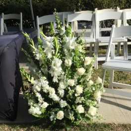 White floral arrangement with roses and tall blooms at an outdoor ceremony