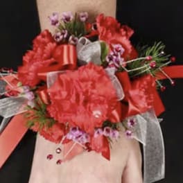 Red floral wrist corsage with ribbons on a person's wrist