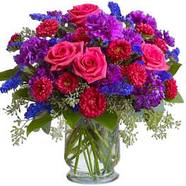 Bouquet of pink roses, purple flowers, and blue accents in a glass vase
