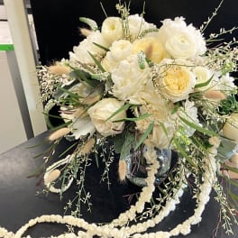 Cream and white floral arrangement in a glass vase with trailing accents