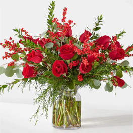 Red roses arranged in a clear glass vase with red berry branches