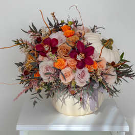 Floral arrangement in a white pumpkin container with roses and orchids