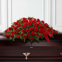 Red rose and carnation casket spray with ribbon on a dark casket
