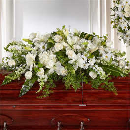 White floral casket spray with lilies and roses on a wooden casket