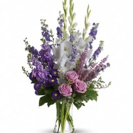 Tall arrangement of white and purple flowers with lavender roses in a clear glass vase