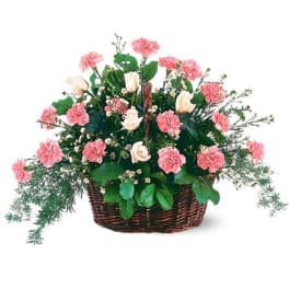 Basket arrangement of pink carnations and pale roses with small white blooms.