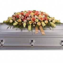 Pastel peach and yellow floral casket spray arranged on a silver casket