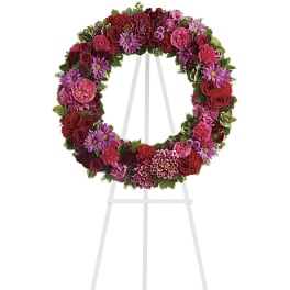 Circular floral wreath on a white easel with pink, purple, and red blooms