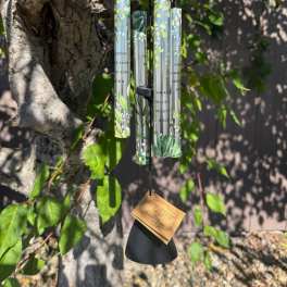 Black wind chime hanging from a tree with printed tubes and a tag