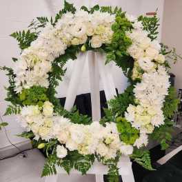 Large white and green standing wreath of roses and mums on a white easel.