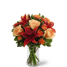 Clear glass vase with peach roses, orange spray roses, and red lilies.