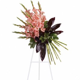 Asymmetrical standing spray of pink flowers with dark leaves and green stems on a white easel