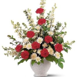 Tall arrangement of red carnations and cream flowers in a white urn-style vase