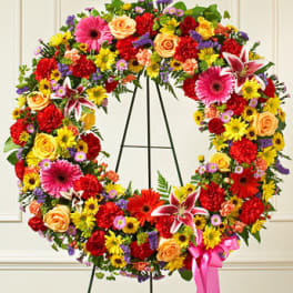 Bright multicolor standing wreath of mixed flowers on a metal easel with a pink ribbon bow