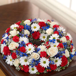 Round wreath of red carnations, white roses and daisies, and blue flowers in a patriotic color palette