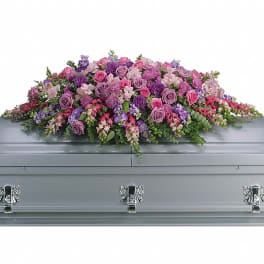 Lavender and pink casket spray of roses and mixed flowers displayed on a silver casket