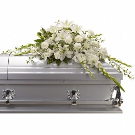 White lily and carnation casket spray arranged on top of a closed silver casket