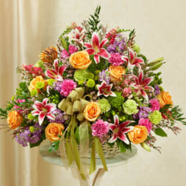 Fan-shaped basket arrangement of pink lilies, peach roses, green mums, and mixed flowers with a ribbon bow