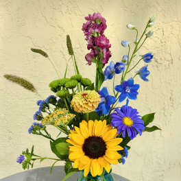 Mixed bouquet in a blue glass mason jar with a sunflower and blue flowers