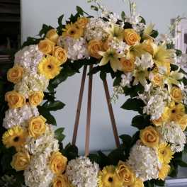 Yellow roses and white flowers arranged in a large wreath on an easel