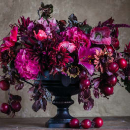 Deep pink and burgundy floral arrangement in a black pedestal vase