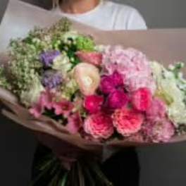 Handheld bouquet of pink, white, and purple flowers wrapped in paper